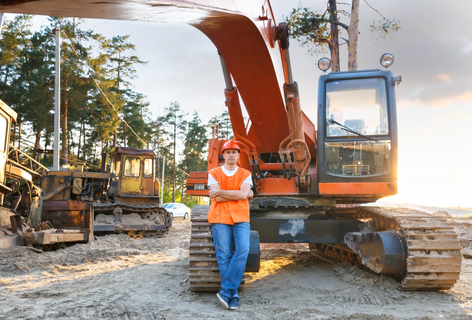 A construction worker in a high-visibility vest and hard hat standing beside a tracked excavator at a worksite.